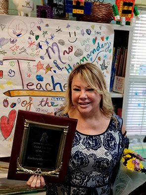2023-2024 Teacher of the Year Ms. Barbara Hernandez with her award in front of homemade teacher of the year banner 